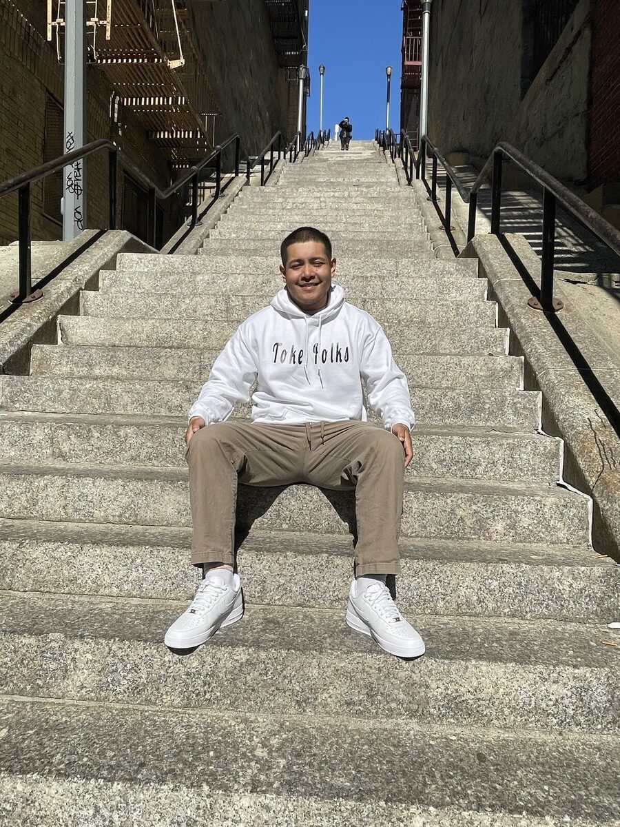 Sitting on city stairs in a white Toke Folks hoodie